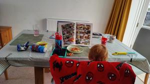 A table with a small boy eating lunch and reading a Dandy annual 